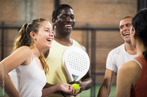 Portrait of young female paddle tennis player during cheerful conversation to her friends on indoor court after game