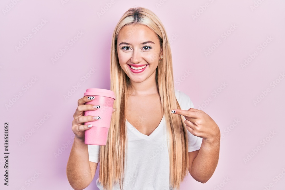 Young blonde girl holding coffee smiling happy pointing with hand and finger Young blonde girl holding coffee smiling happy pointing with hand and finger