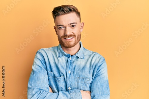 Young redhead man wearing casual denim shirt happy face smiling with crossed arms looking at the camera. positive person.