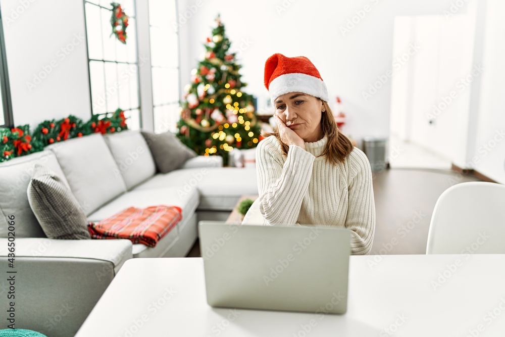 Middle age woman wearing santa claus hat using laptop thinking looking tired and bored with depression problems with crossed arms. Middle age woman wearing santa claus hat using laptop thinking looking tired and bored with depression problems with crossed arms.
