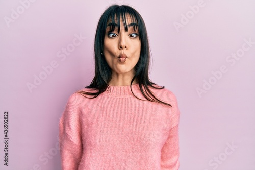 Young brunette woman with bangs wearing casual winter sweater making fish face with lips, crazy and comical gesture. funny expression. © Krakenimages.com