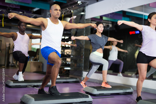 Athletic people performing step aerobics in fitness club