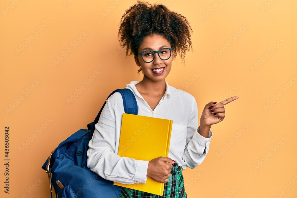 Beautiful african american woman with afro hair wearing school bag and holding books smiling happy pointing with hand and finger to the side Beautiful african american woman with afro hair wearing school bag and holding books smiling happy pointing with hand and finger to the side