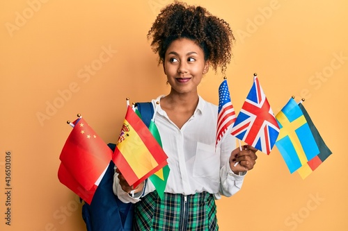 Beautiful african american woman with afro hair exchange student holding countries flags smiling looking to the side and staring away thinking. photo