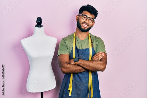Arab man with beard dressmaker designer wearing atelier apron happy face smiling with crossed arms looking at the camera. positive person.