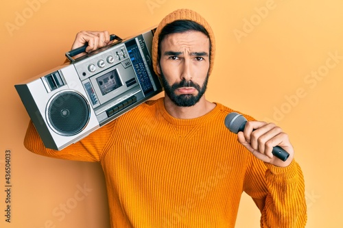 Young hispanic man holding boombox, listening to music singing with microphone depressed and worry for distress, crying angry and afraid. sad expression.