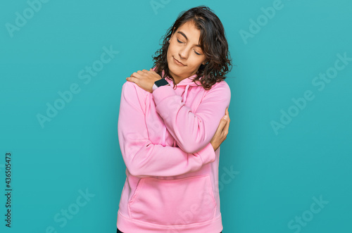 Young hispanic woman wearing casual sweatshirt hugging oneself happy and positive, smiling confident. self love and self care