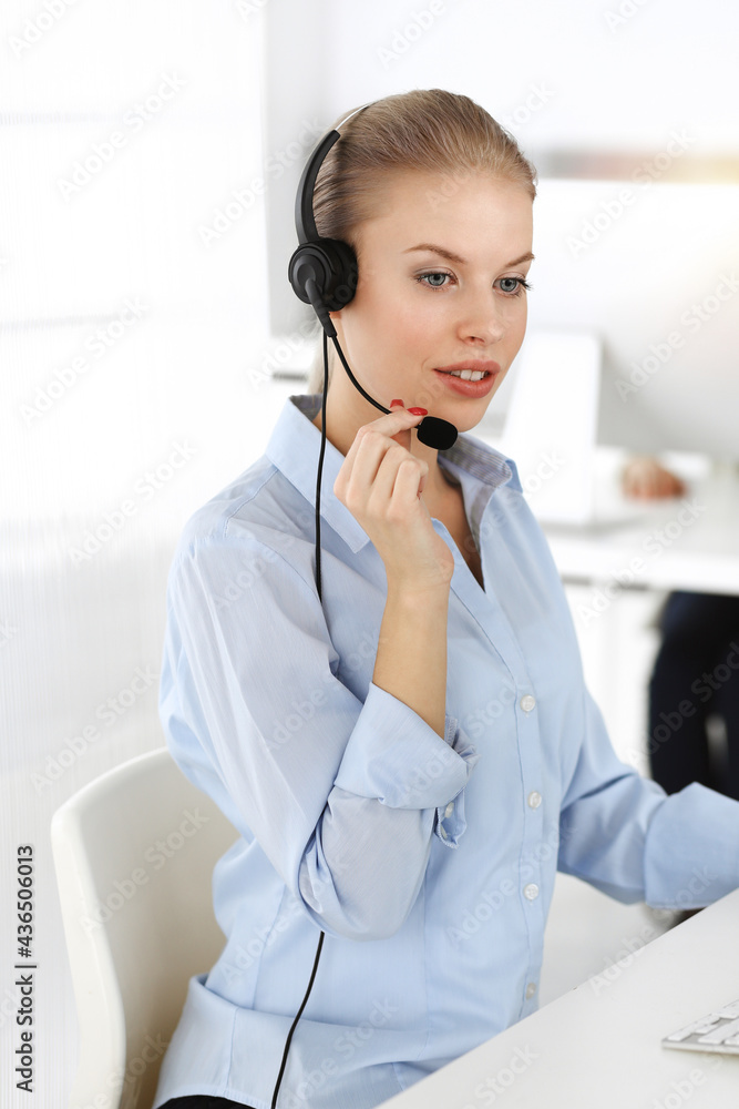 Blond woman working in sunny call center. Group of diverse people working as customer service occupation. Business concept Blond woman working in sunny call center. Group of diverse people working as customer service occupation. Business concept