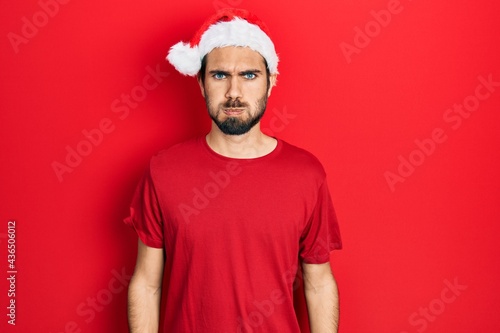 Young hispanic man wearing christmas hat puffing cheeks with funny face. mouth inflated with air, crazy expression.