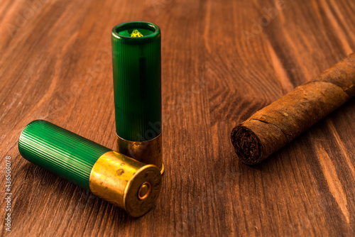 Two 12 gauge bullets and cuban cigar lying on a wooden table. Focus on the cuban cigar