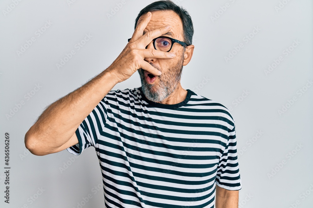 Middle age hispanic man wearing casual clothes and glasses peeking in shock covering face and eyes with hand, looking through fingers afraid Middle age hispanic man wearing casual clothes and glasses peeking in shock covering face and eyes with hand, looking through fingers afraid