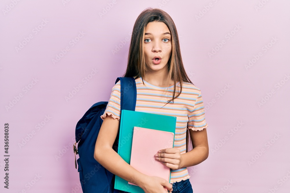 Young brunette girl holding student backpack and books scared and amazed with open mouth for surprise, disbelief face Young brunette girl holding student backpack and books scared and amazed with open mouth for surprise, disbelief face