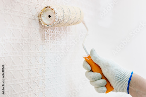 A gloved hand and a paint roller paint the wall in beige. The concept of renovation of premises. Close-up