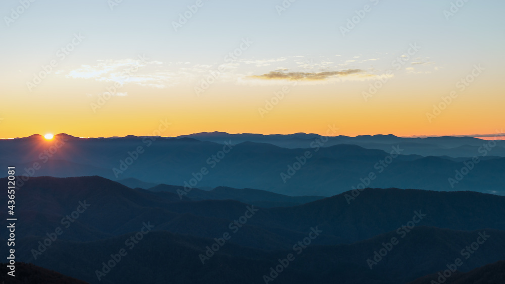Panoramic landscape of blue layers of the Smoky Mountains, as the sun rises from behind the peaks giving the sky an orange blue hue. Taken from Clingman's Dome, Great Smoky Mountains National Park. 