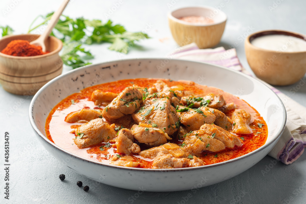 Chicken stew with paprika, onion and sour cream in plate on concrete background. Traditional Hungarian dish Paprikash.