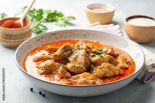 Chicken stew with paprika, onion and sour cream in plate on concrete background. Traditional Hungarian dish Paprikash.