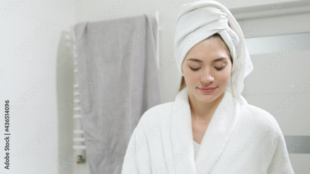 Portrait of young beautiful woman in white robe standing in front of the mirror and brushing teeth. Concept of body care at home or hotel with good mood and modern interior. Portrait of young beautiful woman in white robe standing in front of the mirror and brushing teeth. Concept of body care at home or hotel with good mood and modern interior.