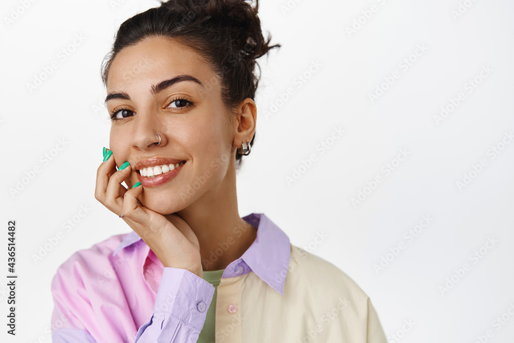 Skin care and women concept. Young attractive woman with clean natural skin, no make up, smiling white teeth, touch cheek and look satisfied at camera, white background Skin care and women concept. Young attractive woman with clean natural skin, no make up, smiling white teeth, touch cheek and look satisfied at camera, white background