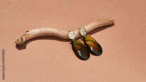 Studio shot of dangle earrings made of golden metal and brown amber epoxy resin on wooden stick isolated over beige background photo