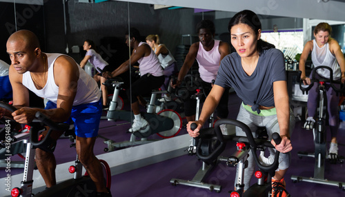 Sporty women and men doing cardio exercises training on stationary bikes at fitness center