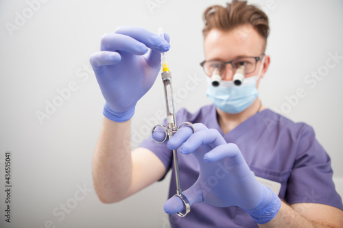 Selective focus on syringe in hands of male doctor, wearing microscope glasses