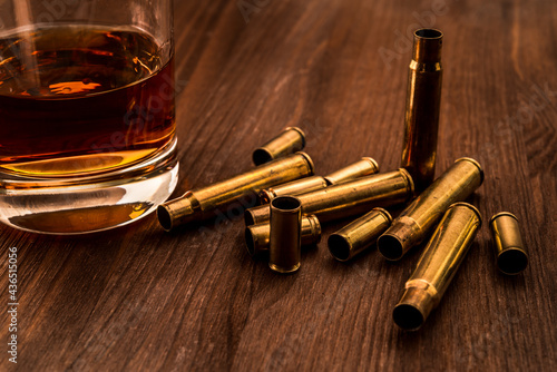 Empty shells from the weapons with glass of whiskey on a wooden table