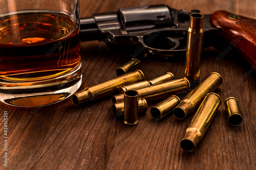 Empty shells from the weapons with glass of whiskey and revolver on a wooden table