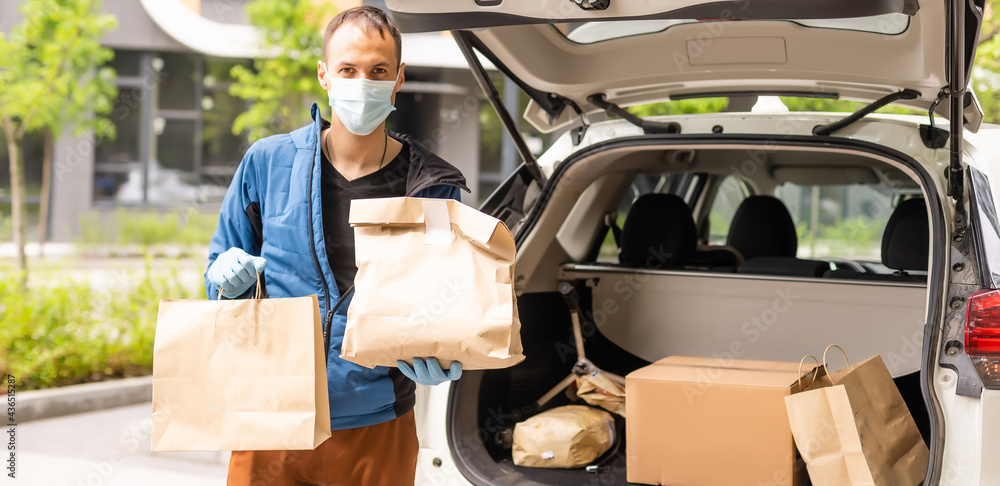 Postal delivery courier man wearing protective face mask in front of cargo van delivering package holding box due to Coronavirus disease or COVID-19 Postal delivery courier man wearing protective face mask in front of cargo van delivering package holding box due to Coronavirus disease or COVID-19