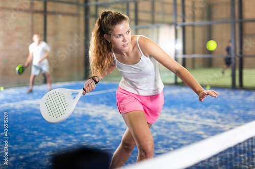 Young sporty woman padel player hitting ball with a racket on a hard court © JackF