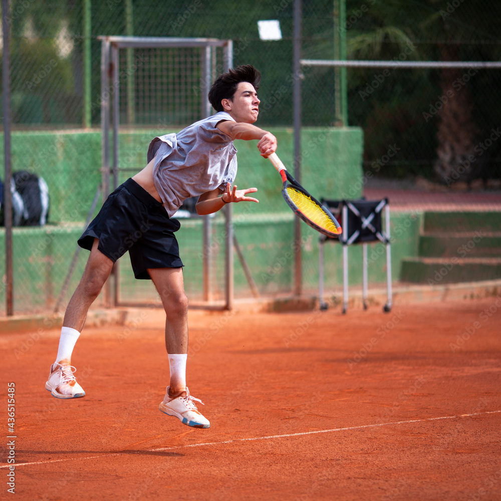 Joven jugador de tenis ejecutando golpe de saque en pista de tierra batida