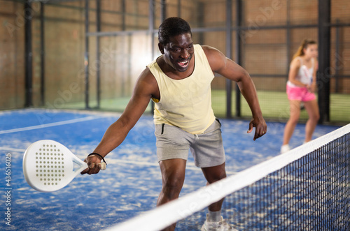 African male player ready to hits the ball while playing padel on a hard court © JackF