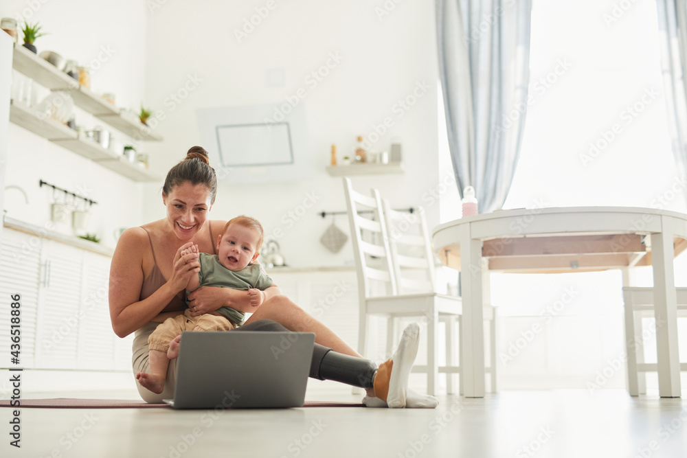 Full length portrait of modern mother with disability holding baby and waving while chatting by video call, copy space Full length portrait of modern mother with disability holding baby and waving while chatting by video call, copy space