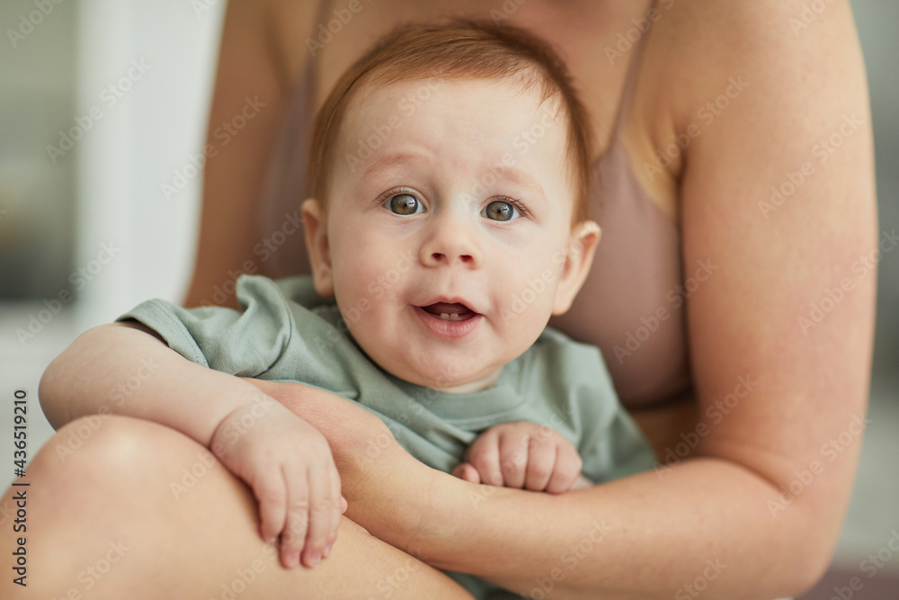 Candid portrait of cute red haired baby looking at camera with loving mother embracing him tenderly