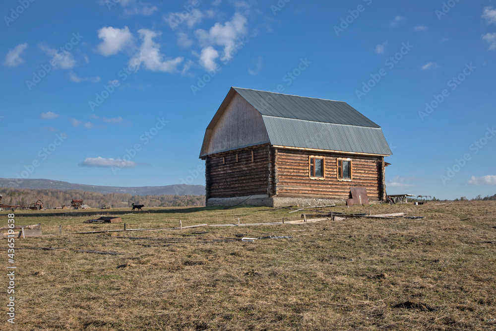 An old wooden house stands against the backdrop of mountains and forests. Rustic rural landscape. Beautiful mountains. Blue sky. Sunny day. An old wooden house stands against the backdrop of mountains and forests. Rustic rural landscape. Beautiful mountains. Blue sky. Sunny day.