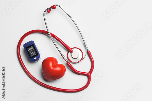 Red heart with pulse oximeter and stethoscope on white background photo