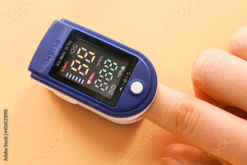 Hand with pulse oximeter on color background photo