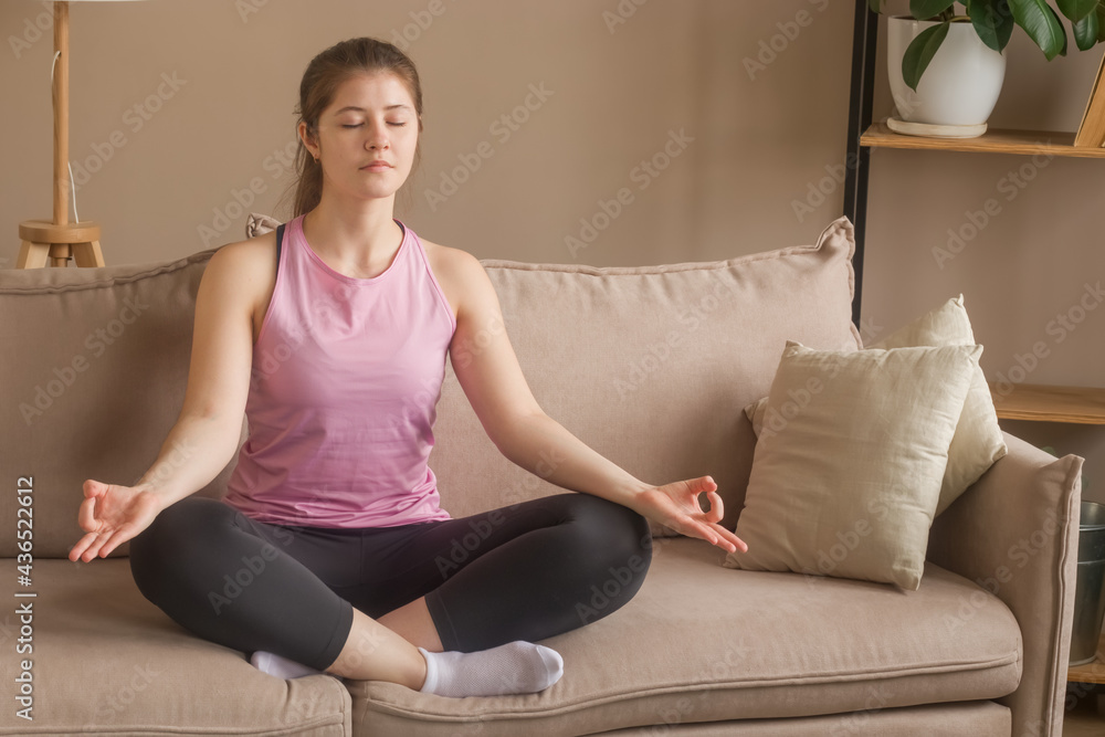 A girl 20-25 does yoga at home. Meditates sitting on the couch. A girl 20-25 does yoga at home. Meditates sitting on the couch.