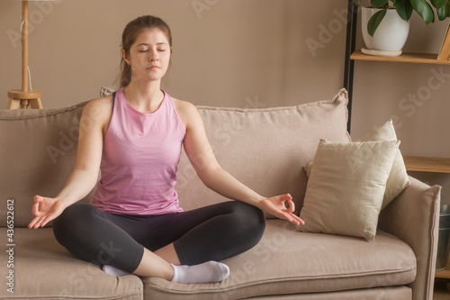 A girl 20-25 does yoga at home. Meditates sitting on the couch.