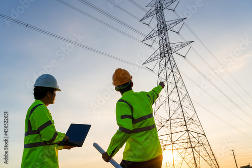 Engineers and Technician working inspections at the electric power station to view the planning work by producing electricity high voltage electric transmission tower at sunset