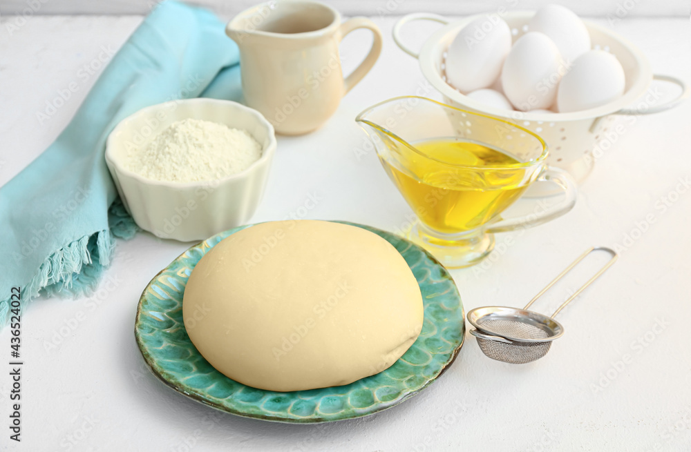 Plate with fresh dough, flour, eggs and oil on light background Plate with fresh dough, flour, eggs and oil on light background