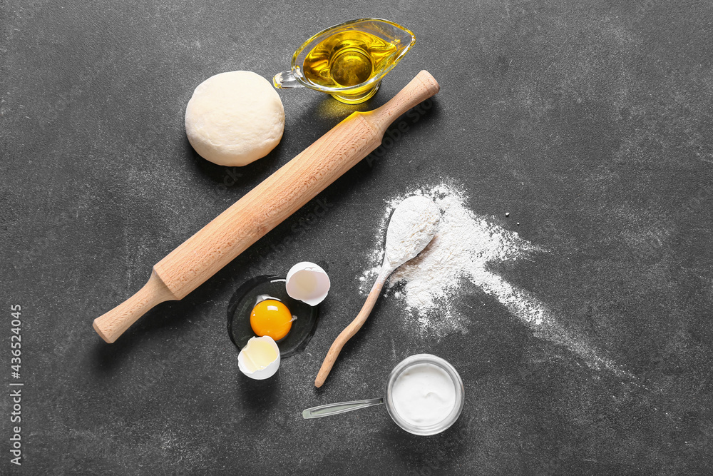 Composition with fresh dough, flour, egg and oil on dark background Composition with fresh dough, flour, egg and oil on dark background