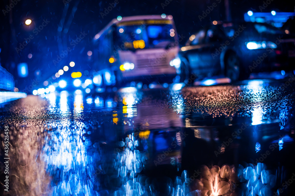Rainy night in the big city, approaching headlights of cars traveling along the avenue. View from the level of the curb on the road