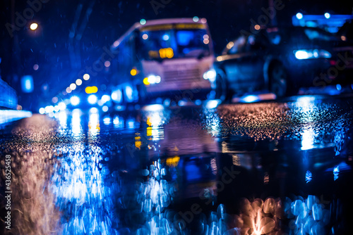 Rainy night in the big city, approaching headlights of cars traveling along the avenue. View from the level of the curb on the road © Georgii Shipin