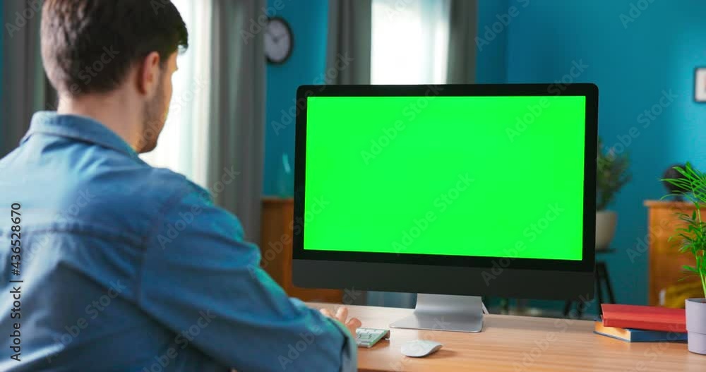 Man Uses all in one computert with blank Screen. Zoom in On a Modern Personal Computer with Mock-up Green Screen Display Standing on the Desk of the Cozy Home Office.