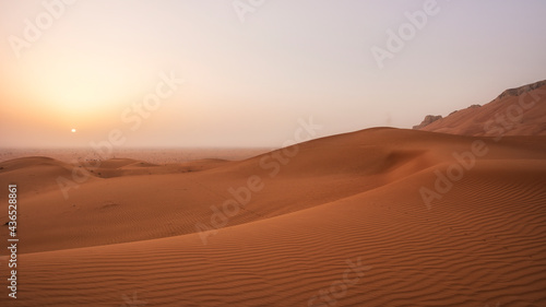 Beautiful desert sunrise with sun visible and sand dooms with sand pattern.