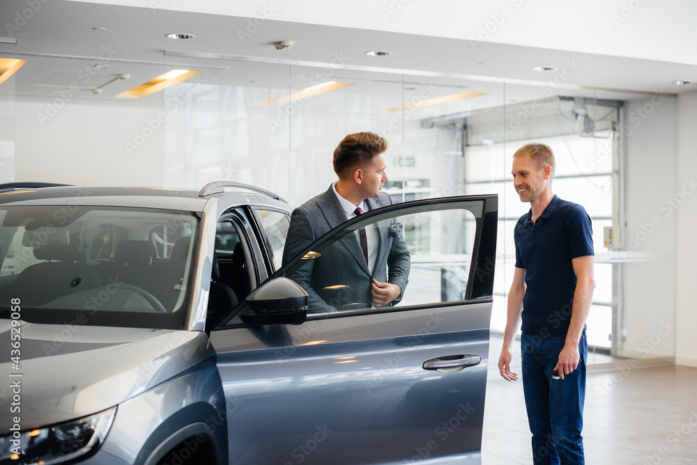 A young businessman with a salesman looks at a new car in a car dealership. Buying a car A young businessman with a salesman looks at a new car in a car dealership. Buying a car