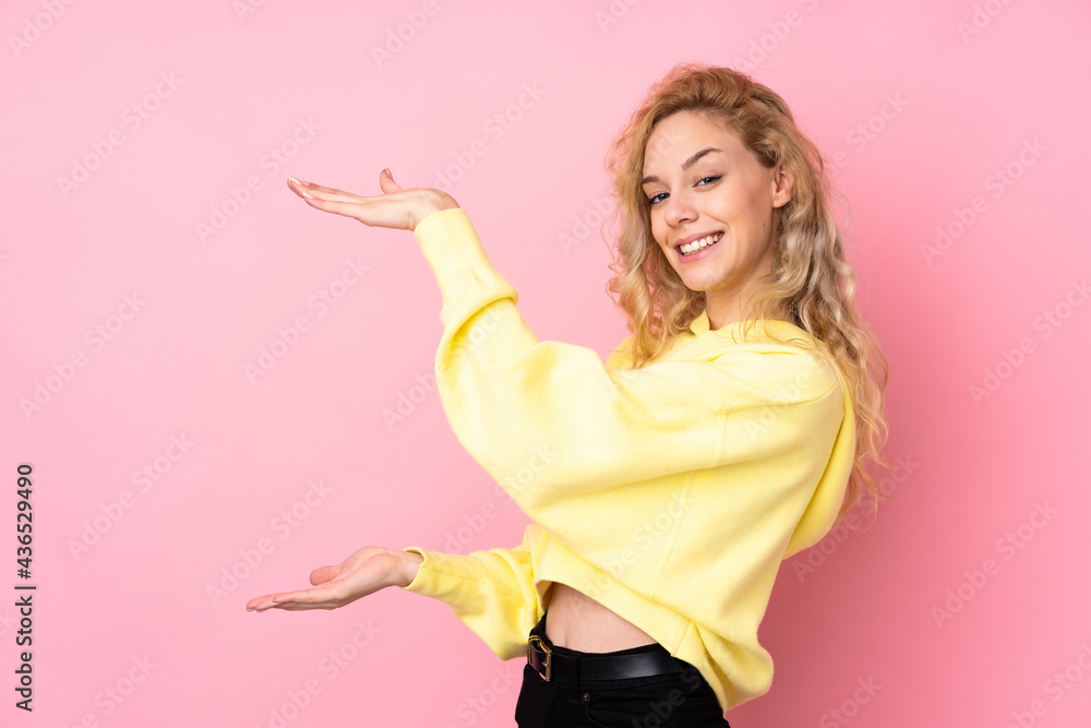 Young blonde woman wearing a sweatshirt isolated on pink background holding copyspace to insert an ad Young blonde woman wearing a sweatshirt isolated on pink background holding copyspace to insert an ad