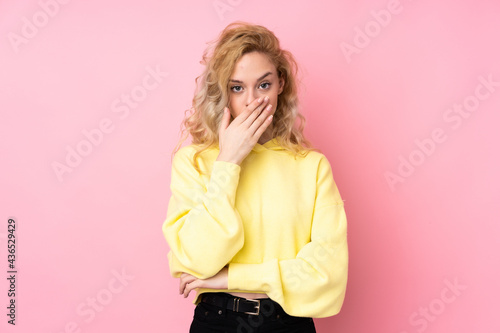 Young blonde woman wearing a sweatshirt isolated on pink background covering mouth with hands