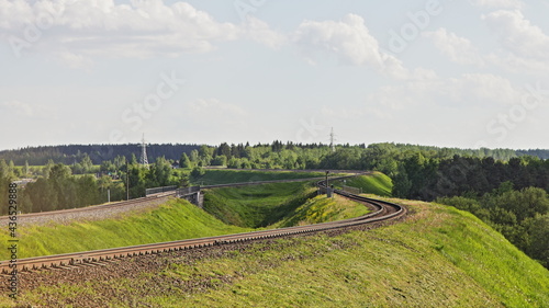 One way railway track turn on green hill on forest trees on horison background  European suburban landscape