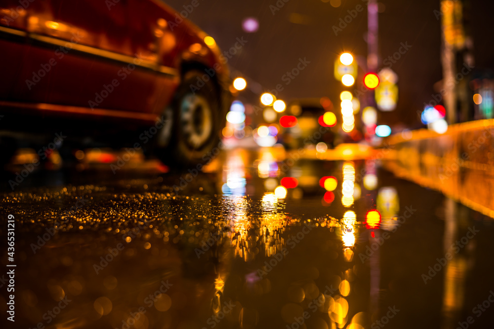 Rainy night in the big city, car passing nearby. View from the level of the puddles near the border